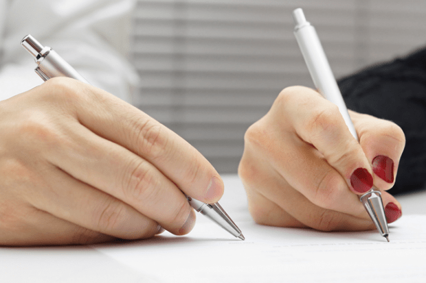 Two hands holding pens, illustrating co-authorship