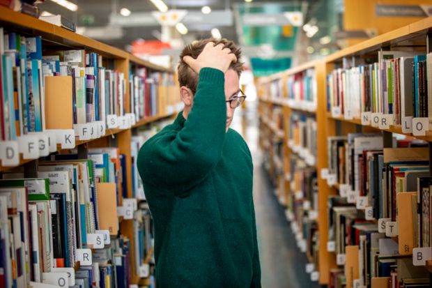 A man looks confused in a library aisle A man looks confused in a library aisle