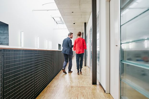 Older man and woman in university corridor, illustrating staff-student relationships.