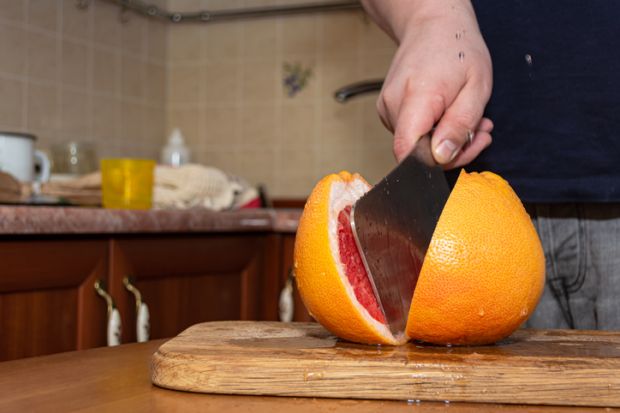Cutting a grapefruit with a kitchen hatchet on a wood board
