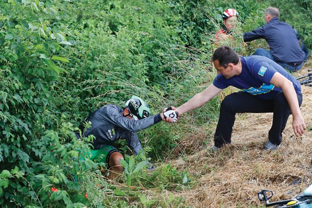 Two men helping cyclists who fell off their bikes Two men helping cyclists who fell off their bikes