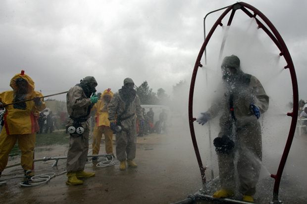 A person in a chemical protection suit walks through a decontamination shower as another is washed down during a mock chemical attack. To illustrate researchers might need to demand retraction of their own papers to decontaminate scientific literature.