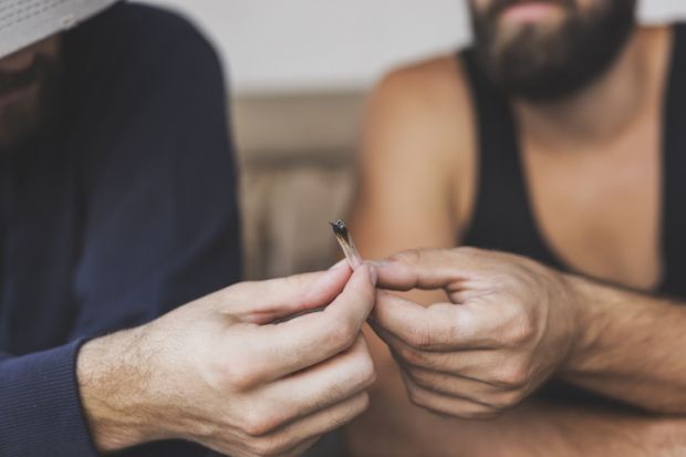 Detail of two men sitting on a couch, sharing a joint, smoking pot