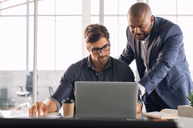 A man points to a computer screen to explain something to another man 