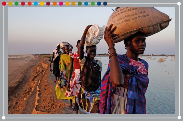 A group of women walk along a dyke protecting Internally Displaced Persons (IDPs), and their host community, from further flooding in Bentiu, South Sudan, 2023. Climate change has divided South Sudan into land that is experiencing flood or drought.