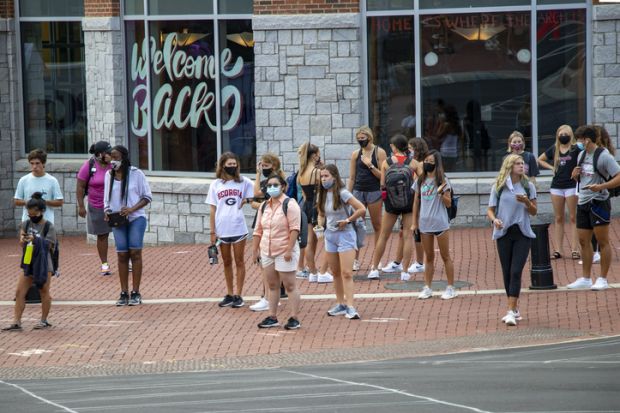 Athens, Georgia - August 20, 2020 During the COVID-19 pandemic on the first day of the Fall semester, students in protective face masks gather at a crossing light in front Bolton Dining Commons at the University of Georgia.