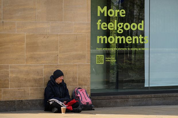 A homeless man begging with a sign next to him advertising “more feelgood moments”. To illustrate that universities are being asked to commit to break down barriers to opportunity and support the government’s mission to drive growth