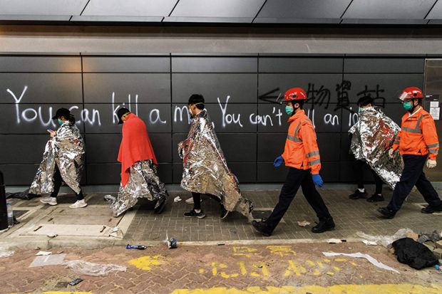 Hong Kong students walk past graffiti