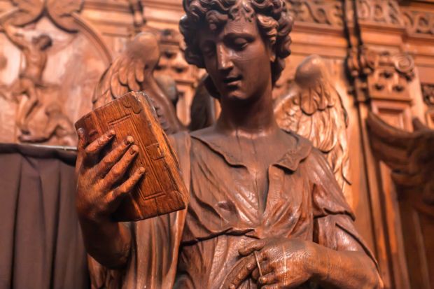 Reading angel holding an old book, wooden statue in 17th century catholic church Saint Charles Borromeo on March 31, 2018.