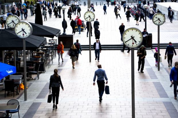 Business people walking in Canary Wharf by the iconic clock installation on Reuters plaza, London's financial district.