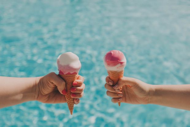 Two hands hold two ice creams by a pool Two hands hold two ice creams by a pool