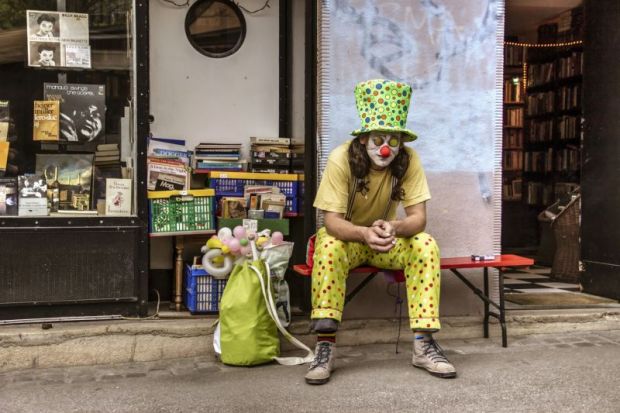 A man in a clown costume sitting and smoking cigarettes in front of an antique bookstore. A man in a clown costume sitting and smoking cigarettes in front of an antique bookstore.