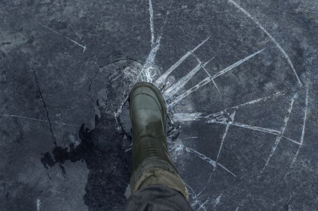 Fisherman foot on broken cracked thin ice at lake