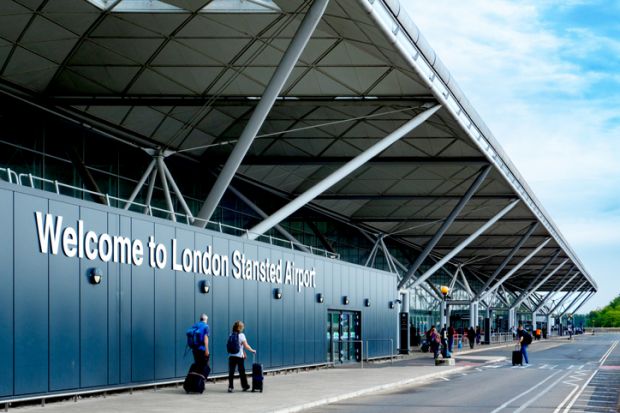Passengers with luggage walking towards the entrance of London Stansted Airport Passengers with luggage walking towards the entrance of London Stansted Airport