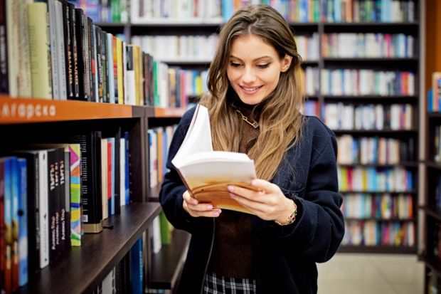 A stock image of a woman reading a book in a library 