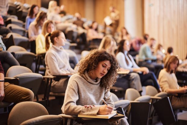 Female student writing in notebook in busy lecture theatre