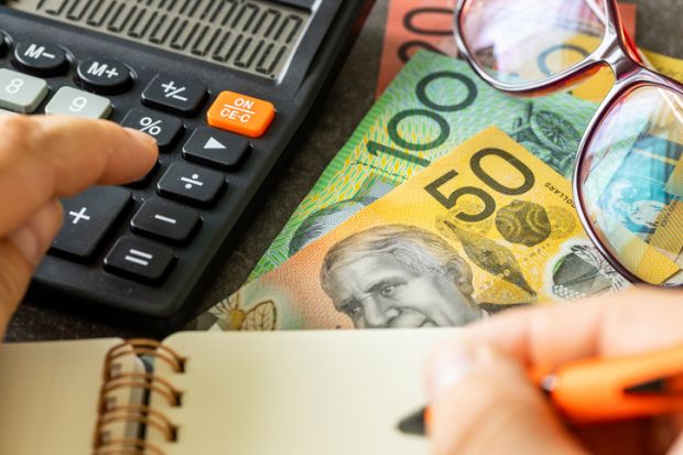 Australian dollars together with a calculator, hand writing down the results in a notebook Australian dollars together with a calculator, hand writing down the results in a notebook