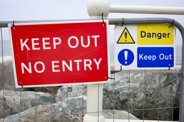 Red and blue 'Keep Out' signs on a fence by the sea