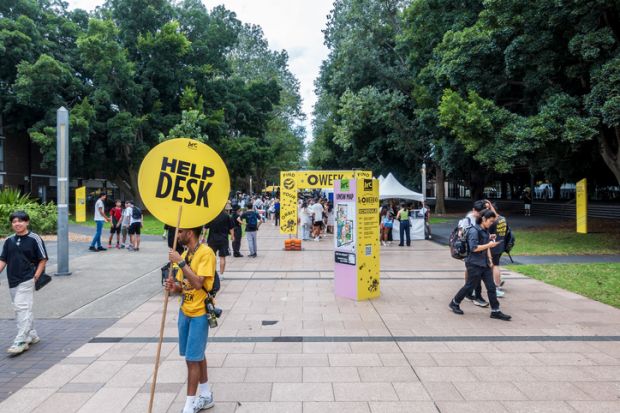 Volunteer student holding a sign offering assistance to visitors on University of New South Wales (UNSW) Orientation Week (O Week)