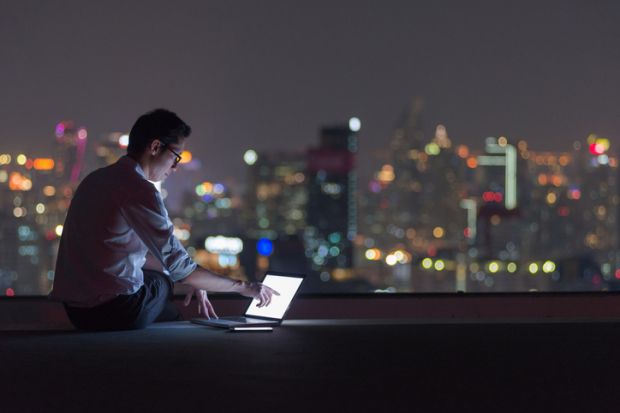 A man in a dark room overlooking a cityscape at night uses a laptop A man in a dark room overlooking a cityscape at night uses a laptop