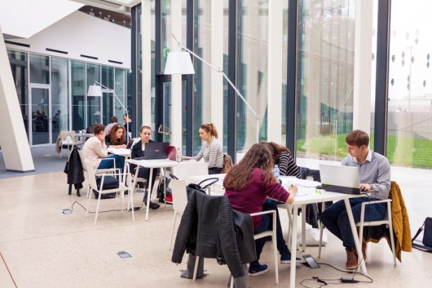 Young adult students sitting in groups in modern library and studying.