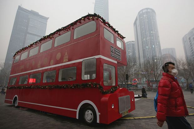 A man wearing mask passes a London double-decker bus model during a heavy pollution day in Beijing, China. Illustrating transnational education (TNE). A man wearing mask passes a London double-decker bus model during a heavy pollution day in Beijing, China. Illustrating transnational education (TNE).