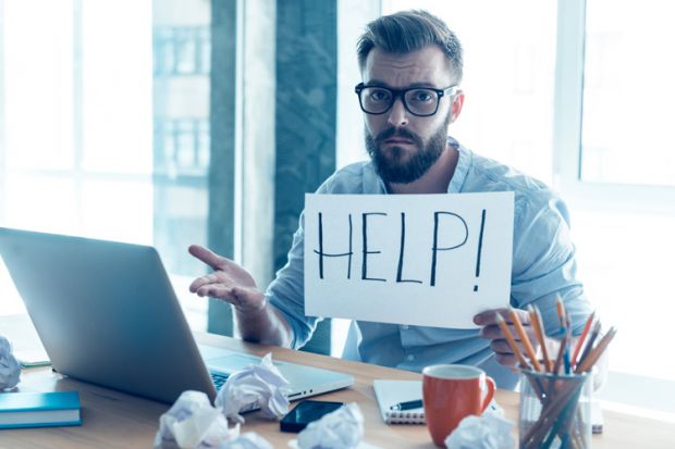 Man at desk holding 'Help' sign Man at desk holding 'Help' sign