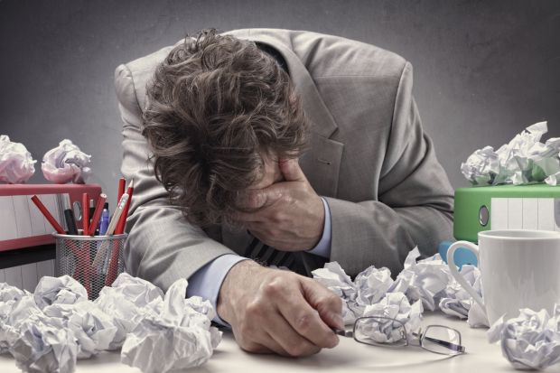 Man with head in hand surrounded by paper Man with head in hand surrounded by paper