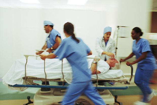 Four medics pushing mature male patient through hospital corridor on trolley. Four medics pushing mature male patient through hospital corridor on trolley.