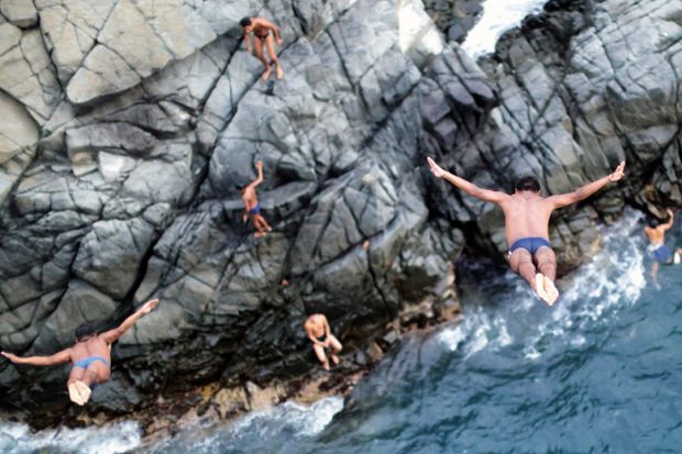 Men diving off cliff into sea Men diving off cliff into sea