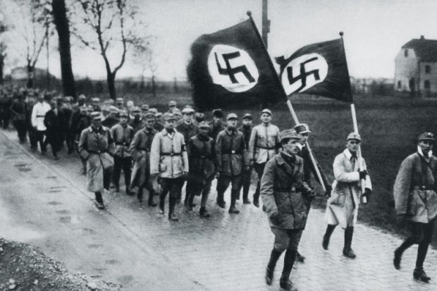 Men marching behind flags with swastikas on them Men marching behind flags with swastikas on them