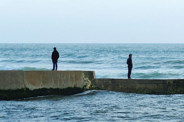 Men standing in opposite directions on seafront wall Men standing in opposite directions on seafront wall
