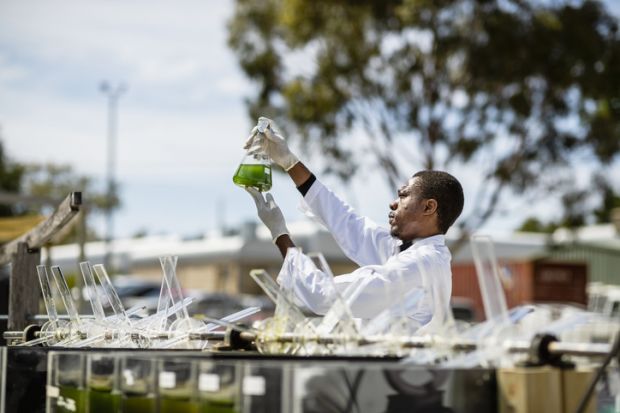 A young scientist working on research outdoors, holding up a glass beaker and inspecting the liquid inside, symbolising open science 