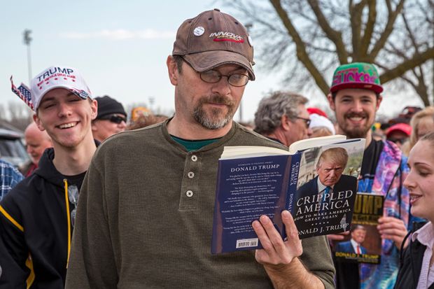 A man reads a Donald Trump book while waiting in a long line for admission to a Trump campaign rally, 2016. To illustrate that academics might need to 'tread carefully' with courses on Trump. A man reads a Donald Trump book while waiting in a long line for admission to a Trump campaign rally, 2016. To illustrate that academics might need to 'tread carefully' with courses on Trump.