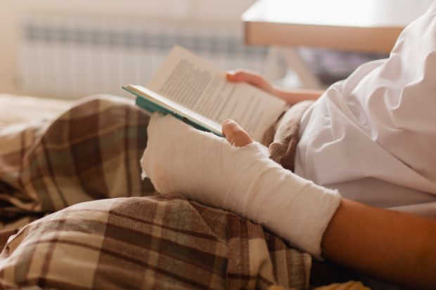 A person reads a book with a bandaged arm, symbolising the scarring PhD experience A person reads a book with a bandaged arm, symbolising the scarring PhD experience