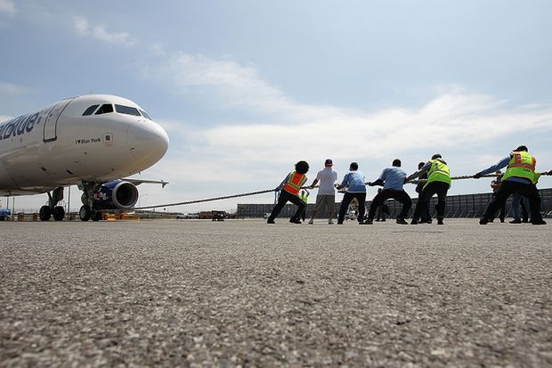 A team of people try to pull a 150,000 pound aircraft, illustrating the extra burden on universities from the UK government’s proposed levy on international student fees.