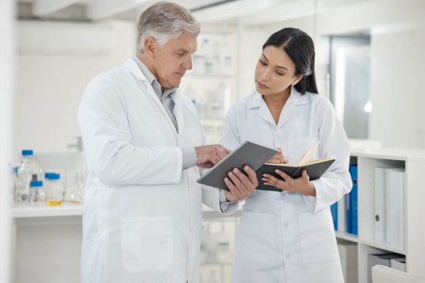 A senior scientist shows a junior scientist something on a tablet A senior scientist shows a junior scientist something on a tablet