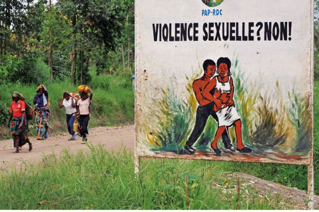 Congolese women walk past a sign opposing sexual violence Congolese women walk past a sign opposing sexual violence