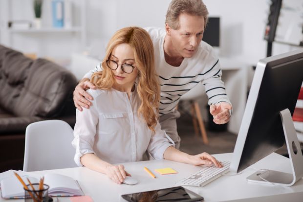 A man touches a woman's shoulder as she works on her computer A man touches a woman's shoulder as she works on her computer, symbolising sexual harassment