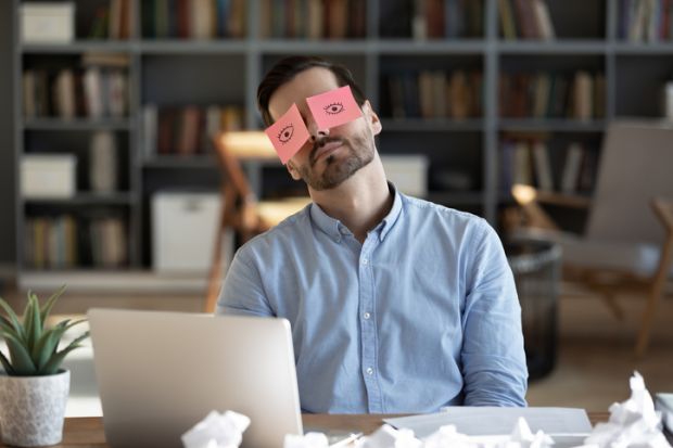 A business person sleeps with post-it notes of open eyes on his eyes A business person sleeps with post-it notes of open eyes on his eyes