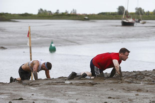 People crawling through the mud at the Maldon Mud Race, UK. To illustrate frustration at the lack of career progression within UK universities due to promotion freezes.