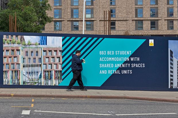A member of the public walks past a bright and colourful construction hoarding advertising a development of rental student accommodation with shared amenity spaces and retail units in Leeds, UK
