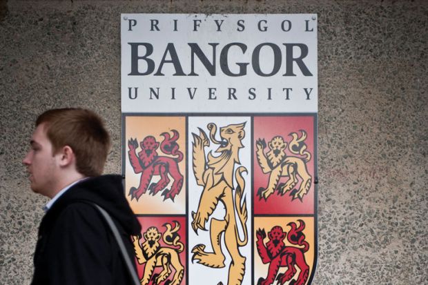 Student walking by Bangor University crest shield logo Student walking by Bangor University crest shield logo