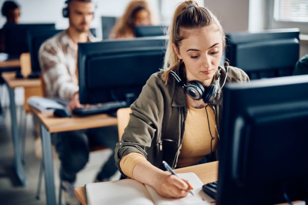 A university student writes notes while e-learning on a computer in the classroom