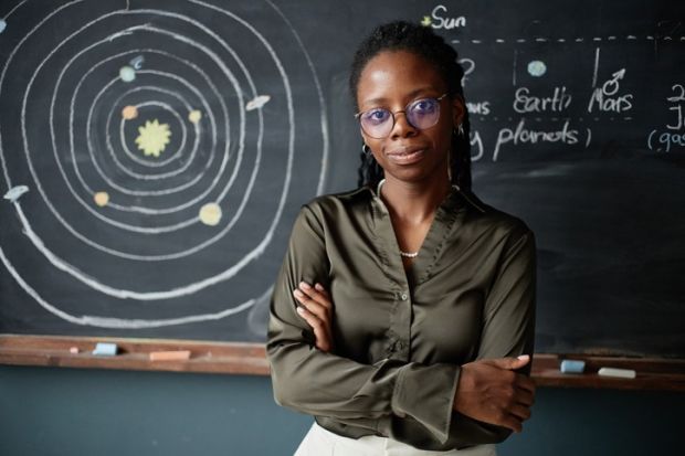 A black physics teacher stands in front of the blackboard