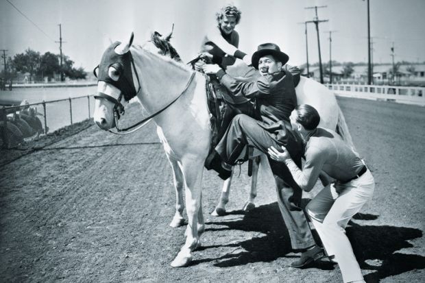 Young couple trying to help a man get onto his horse
