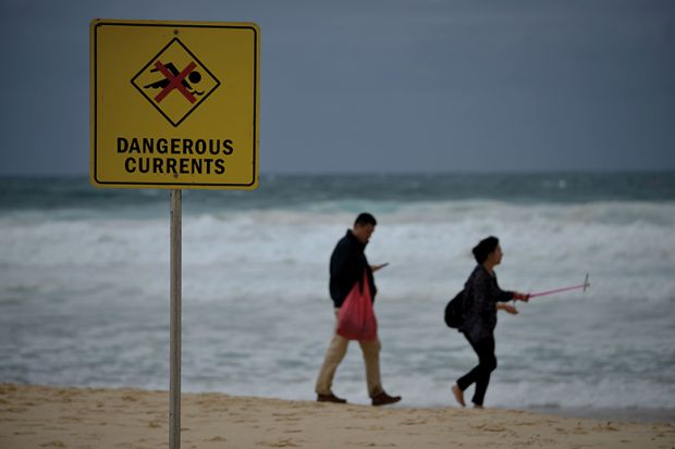 Visitors walk on Bondi beach next to a warning sign for dangerous sea currents on a stormy day in Sydney Visitors walk on Bondi beach next to a warning sign for dangerous sea currents on a stormy day in Sydney