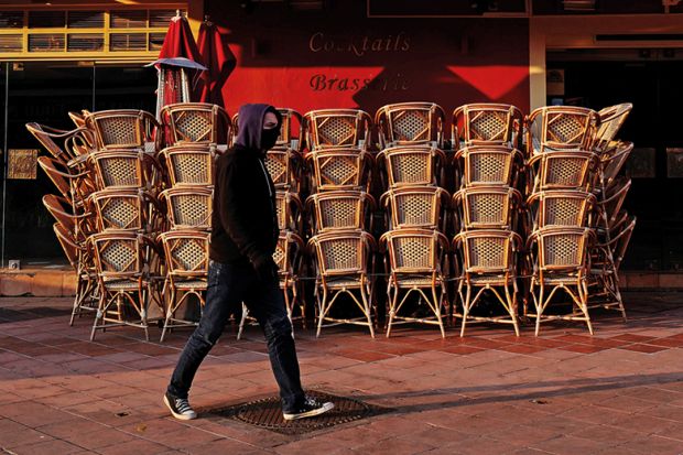 Man with facemask walking past closed cafe during coronavirus pandemic. France.