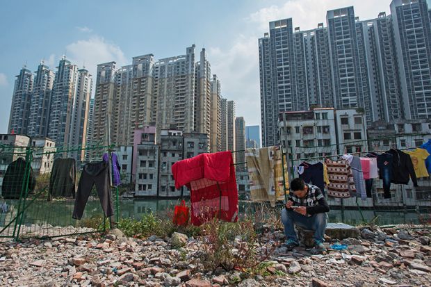 A man sits on a rock near demolished residential buildings in Xiancun, an urban village in the Zhujiang New Town district of Guangzhou as high commercial and residential buildings rise in the distance