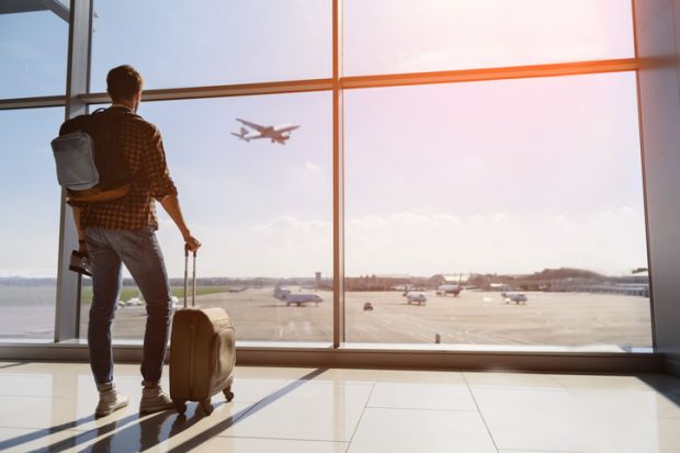 A traveller with a suitcase looks out from an airport terminal building at a plane taking off A traveller with a suitcase looks out from an airport terminal building at a plane taking off